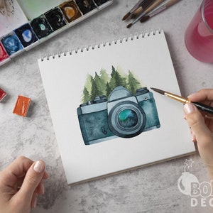 May include: A watercolor painting of a vintage camera with a green forest background. The camera is painted in shades of gray and blue, with a green lens. The forest is painted in shades of green and brown.