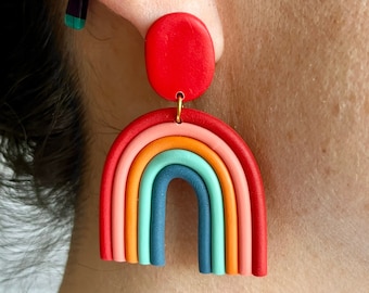 Könnte beinhalten: Ein Paar regenbogenfarbene Ohrringe aus Ton mit einem roten Kreis oben. Die Ohrringe haben die Form eines Regenbogenbogens.