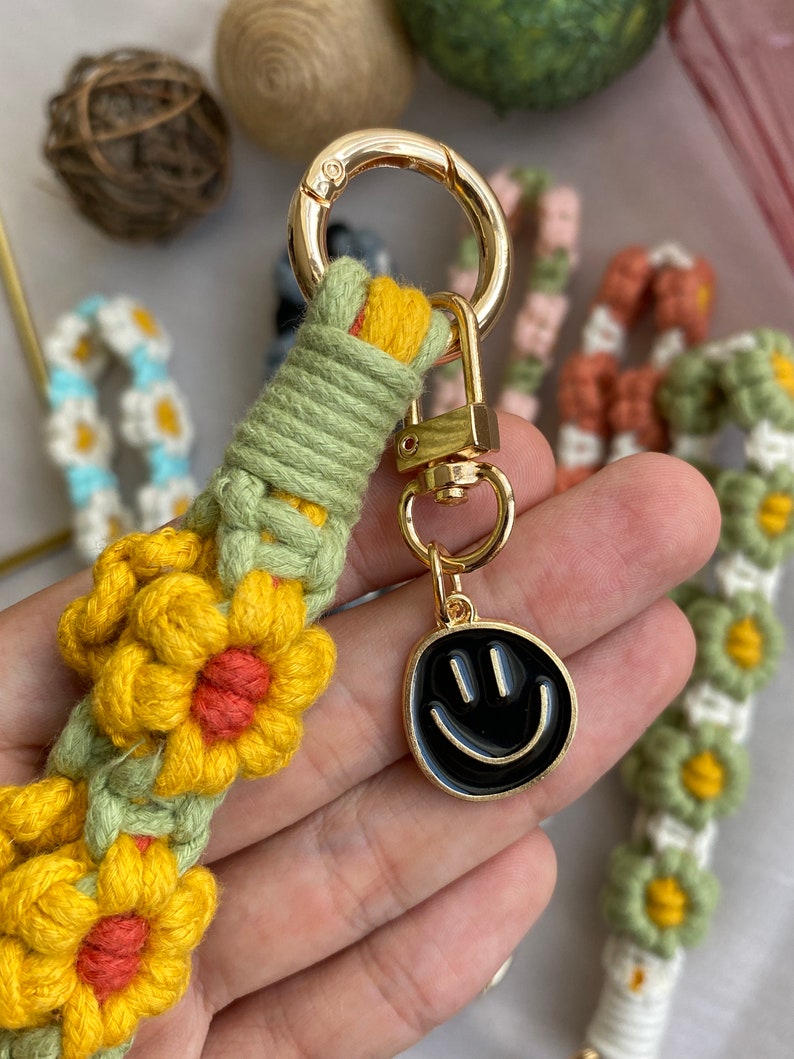 May include: A green, yellow, and orange crocheted keychain with a gold metal ring and a black smiley face charm.