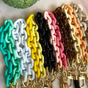 May include: A set of colorful plastic chain links with gold clasps. The chains are in shades of green, white, yellow, black, pink, orange, and beige.