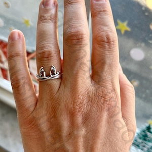 May include: A silver ring featuring a stylized antler design. The ring is worn on a finger, showcasing the intricate details of the antler shape. The ring's design is simple yet elegant, suitable for everyday wear.