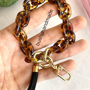 May include: A brown and gold chain keychain with a black tassel. The chain is made of large, chunky links with a tortoise shell pattern. The keychain has a gold clasp and a gold ring.
