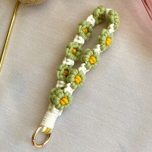 May include: A green and white crocheted keychain with a gold metal ring. The keychain is decorated with small yellow flowers.