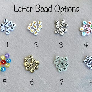 Puede incluir: La imagen muestra ocho opciones diferentes de cuentas de letras. Las cuentas son blancas con letras negras, doradas o coloridas. El texto "Letter Bead Options" est&aacute; en la parte superior. Los n&uacute;meros del 1 al 8 est&aacute;n debajo de cada opci&oacute;n de cuentas.