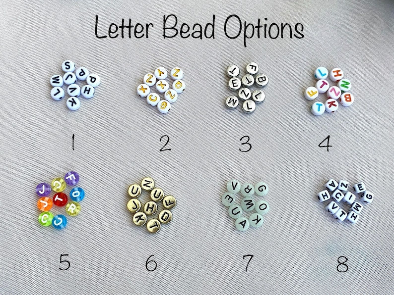 Puede incluir: La imagen muestra ocho opciones diferentes de cuentas de letras. Las cuentas son blancas con letras negras, doradas o coloridas. El texto "Letter Bead Options" est&aacute; en la parte superior. Los n&uacute;meros del 1 al 8 est&aacute;n debajo de cada opci&oacute;n de cuentas.