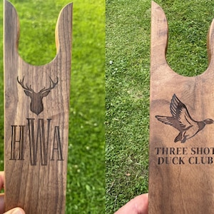 May include: Two wooden boot jacks with engraved designs. The first boot jack has a deer head and the initials "HWA". The second boot jack has a flying duck and the text "THREE SHOT DUCK CLUB".