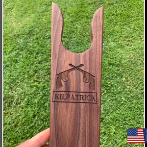 May include: A wooden boot jack with a personalized name "Kilpatrick" and a design of two crossed pistols. Made in the USA.