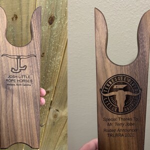 May include: Two wooden boot jacks with engraved designs. The first boot jack has the text "Josh Little Rope Horses Mebane, North Carolina". The second boot jack has the text "Tennessee River Rodeo Association Little Britches Special! Thanks To: Mr. Terry Jobe Rodeo Announcer TRIBRA 2020".
