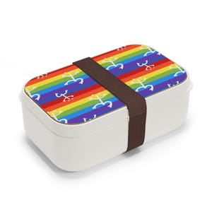 May include: White lunchbox with a rainbow and white symbol pattern on the lid. The lunchbox has a brown strap.