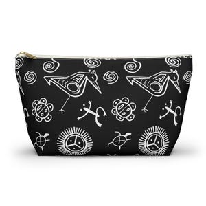 May include: Black zippered pouch with a white repeating pattern of stylized birds, frogs, turtles, and suns. The pattern is inspired by ancient petroglyphs.