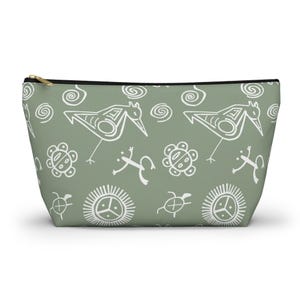 May include: A green zippered pouch with a white pattern of stylized birds, frogs, turtles, and suns. The pattern is inspired by ancient petroglyphs.