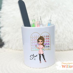 May include: White ceramic cup with a nail technician illustration. The cup features a cartoon of a woman in a pink uniform, holding nail tools. The word "Star" is written on the cup. A nail file and other tools are inside the cup.