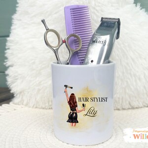 May include: A white ceramic cup with a hair stylist design, holding hair styling tools. The cup features a graphic of a woman holding a hair dryer and brush, with the text "HAIR STYLIST Lily". Inside are scissors, a comb, and a Wahl hair clipper.
