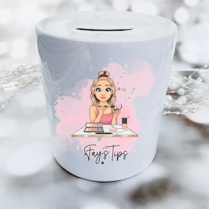 May include: White ceramic money box with a pink and white watercolour design. A cartoon illustration of a woman with blonde hair is applying makeup. The text "Fay's Tips" is printed on the front of the money box.