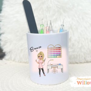 May include: White ceramic pen holder featuring a nail technician illustration. The design includes a nail polish display, a nail table, and the name "Breeze". The holder contains nail tools and a nail file.