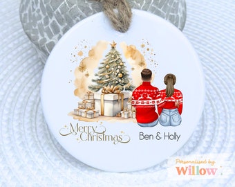May include: White ceramic Christmas ornament with a watercolor design. The ornament features a Christmas tree, wrapped gifts, and a couple wearing matching red sweaters. The text "Merry Christmas" and names are also included.