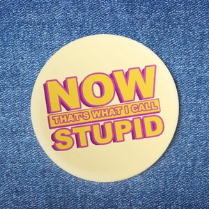 May include: A yellow button with the text "NOW THAT'S WHAT I CALL STUPID" in pink and yellow letters.