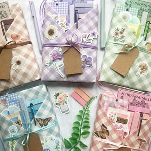 May include: Five gift-wrapped packages with a gingham pattern in various colours, decorated with floral and butterfly stickers, pens, and tags. Each package is tied with a ribbon and contains stationery items. The tags read "MY BOOKISH SHELF".
