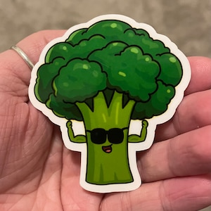 May include: A green cartoon broccoli wearing sunglasses and flexing its arms. The broccoli has a happy expression on its face.