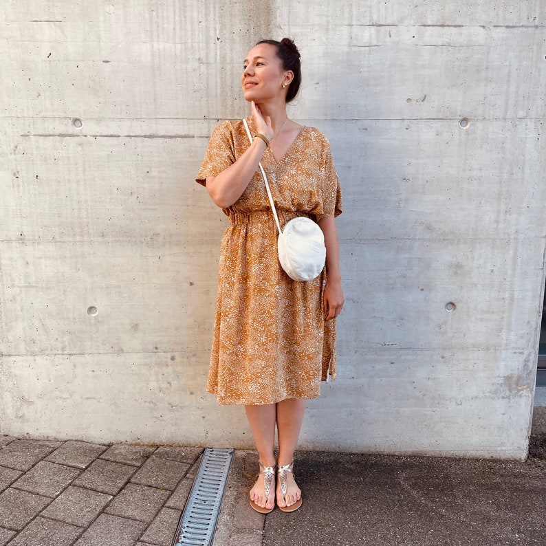 May include: A woman wearing a yellow floral dress with a white round crossbody bag and silver sandals.