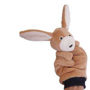 May include: A brown plush bunny hand puppet with a white face and black eyes. The puppet is holding its paws together in front of its chest.