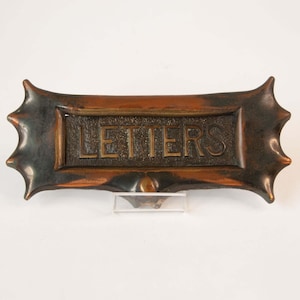 May include: A vintage copper letterbox with a brass plaque that reads "LETTERS". The letterbox has a decorative, spiky design around the edges.
