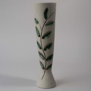 May include: A tall, off-white ceramic vase with a flared base and a narrow top. A green leaf and vine design decorates the front of the vase. The vase is approximately 25 cm tall.