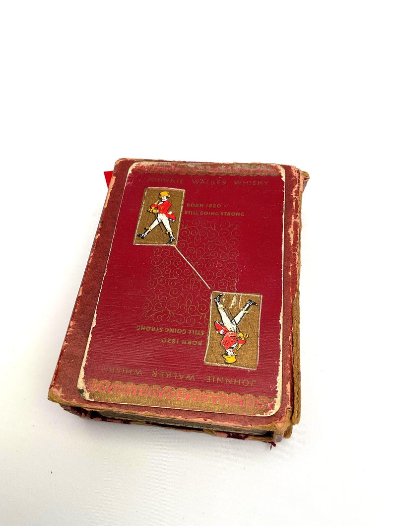 May include: A vintage red and gold Johnnie Walker Whisky booklet. The cover features the text "Johnnie Walker Whisky" and "Born 1820 Still Going Strong." Two illustrations of a man in a red coat are on the cover.