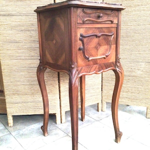 Może przedstawiać: Antyczna drewniana szafka nocna z marmurowym blatem, wyposażona w jedną szufladę i drzwi szafki z misternymi rzeźbami. Szafka nocna ma nogi typu cabriole i bogaty brązowy kolor.