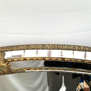 K&ouml;nnte beinhalten: Verzierter, gew&ouml;lbter Spiegelrahmen mit Goldfinish und dekorativen Details. Der Rahmen weist ein mosaikartiges Muster mit rechteckigen Spiegelfliesen auf. Das Design umfasst florale Akzente und eine Vintage-&Auml;sthetik.