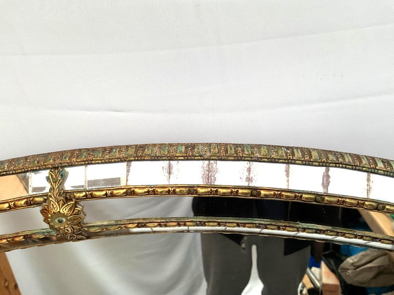 K&ouml;nnte beinhalten: Verzierter, gew&ouml;lbter Spiegelrahmen mit Goldfinish und dekorativen Details. Der Rahmen weist ein mosaikartiges Muster mit rechteckigen Spiegelfliesen auf. Das Design umfasst florale Akzente und eine Vintage-&Auml;sthetik.