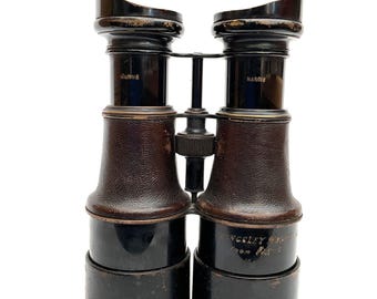 Könnte beinhalten: Vintage schwarzes und braunes Fernglas mit Lederakzenten. Auf dem Fernglas stehen die Wörter "MARINE" und "NARDIE". Auf der Basis des Fernglases steht der Text "KINGSLEY HARVEY" und "FROM PARIS".