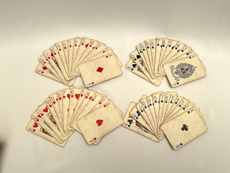 May include: Four fanned decks of playing cards with a vintage aesthetic. Each deck displays a variety of suits and numbers, including hearts, diamonds, clubs, and spades. The cards have a worn, aged appearance.