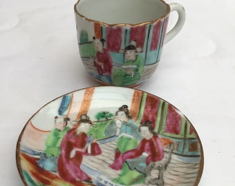 May include: A vintage teacup and saucer set with a hand-painted design of people in traditional Chinese clothing. The set is made of white porcelain with gold accents.