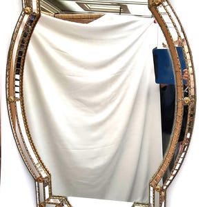 K&ouml;nnte beinhalten: Verzierter, ovaler Spiegel mit goldfarbenem Rahmen. Der Rahmen hat kleine, quadratische Spiegelfliesen und goldfarbene Akzente. Der Spiegel hat ein symmetrisches Design mit Vintage- oder Antik-&Auml;sthetik.