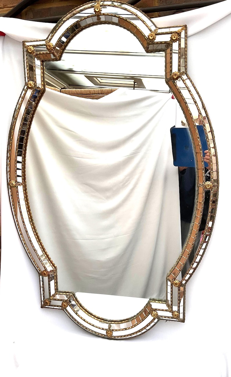 K&ouml;nnte beinhalten: Verzierter, ovaler Spiegel mit goldfarbenem Rahmen. Der Rahmen hat kleine, quadratische Spiegelfliesen und goldfarbene Akzente. Der Spiegel hat ein symmetrisches Design mit Vintage- oder Antik-&Auml;sthetik.