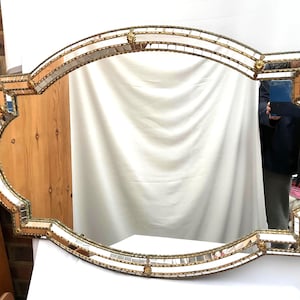 K&ouml;nnte beinhalten: Ein verzierter, gro&szlig;er, rechteckiger Spiegel mit einem dekorativen goldfarbenen Rahmen. Der Rahmen ist mit kleinen Spiegelfliesen und goldenen Akzenten verziert. Die Form des Spiegels ist ein einzigartiges, geschwungenes Design, geeignet f&uuml;r Wanddekoration.