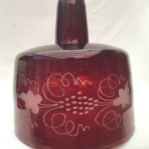 May include: A deep red glass pendant light with a white etched floral design. The light has a wide, round base and a narrow, cylindrical top.