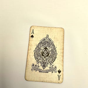May include: Vintage playing card, the Ace of Spades, with a detailed black and white illustration. The card features the word "A" in the corners and an ornate central design with text that reads "Goodall London". The card has a distressed, aged appearance.