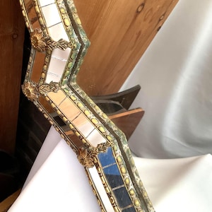 K&ouml;nnte beinhalten: Ein verzierter, antiker Spiegelrahmen mit goldener und gr&uuml;ner Oberfl&auml;che. Der Rahmen ist mit kleinen Spiegelfliesen und dekorativen goldenen Akzenten segmentiert. Der Rahmen hat eine einzigartige, eckige Form und ist vor einem neutralen Hintergrund platziert.