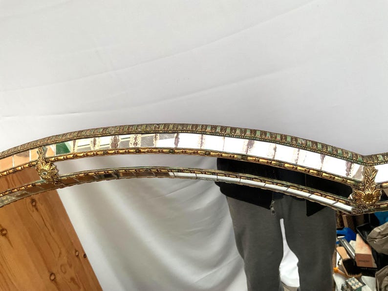 K&ouml;nnte beinhalten: Ein dekorativer Spiegel mit einem goldfarbenen Rahmen und einem Mosaik-Bord. Der Rahmen hat verzierte Details und eine geschwungene Form. Die Oberfl&auml;che des Spiegels ist reflektierend, und das Gesamtdesign ist von Vintage inspiriert.
