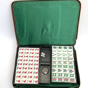 May include: A vintage Mahjong set in a brown zipped case with a green lining. The set contains tiles with red and green symbols, dice, and a circular marker. The tiles are arranged in black trays.