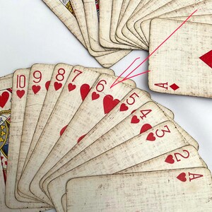 May include: A collection of vintage playing cards, fanned out to display the suits and numbers. The cards feature a cream-colored background with red heart symbols and numbers. The cards are arranged on a white surface.