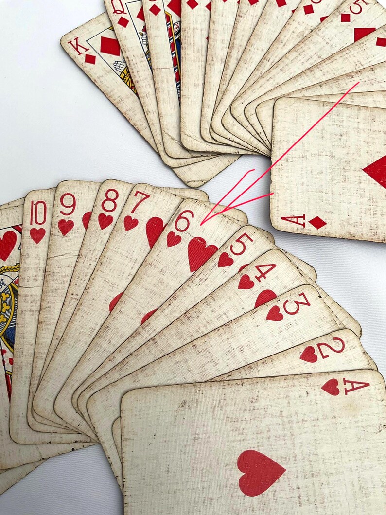 May include: A collection of vintage playing cards, fanned out to display the suits and numbers. The cards feature a cream-colored background with red heart symbols and numbers. The cards are arranged on a white surface.