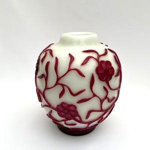 Könnte beinhalten: Eine weiße Glasvase mit rundem Körper und schmalem Hals. Die Vase ist mit einem weinroten Blumendesign verziert. Der Boden der Vase ist dunkelweinrot. Die Vase steht auf einer weißen Oberfläche.