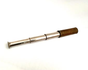 May include: A vintage, extendable telescope with a silver-colored body and a brown, cylindrical eyepiece. The telescope is lying horizontally against a white background. The telescope is a classic nautical or scientific instrument.