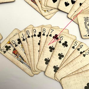 May include: A collection of vintage playing cards, featuring the suits of clubs and spades. The cards have a worn, antique appearance with visible wear and tear. The image showcases various numbered cards, including the six, seven, eight, nine, and ten of clubs.
