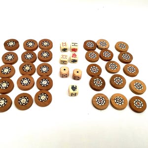 Puede incluir: Un conjunto de piezas de juego de madera, que incluyen fichas redondas con diseños de estrellas incrustadas y varios dados. Las fichas son marrones con detalles en blanco y negro. Los dados son de color marfil y marrón, con varios puntos y símbolos.
