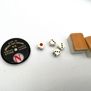 May include: A selection of Mahjong game components, featuring dice, tiles, and a black marker with the text "KWONG FAT CHEUNG H.K." The dice are white with black pips, and the tiles have a light brown top.