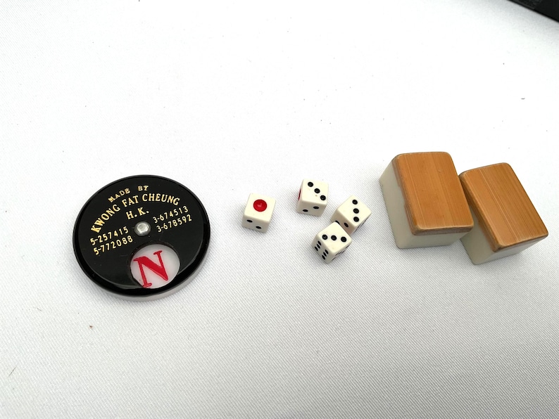 May include: A selection of Mahjong game components, featuring dice, tiles, and a black marker with the text "KWONG FAT CHEUNG H.K." The dice are white with black pips, and the tiles have a light brown top.